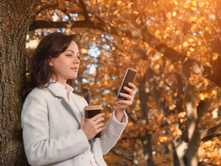 Beautiful woman drinking coffee outdoor and chatting on smartphone