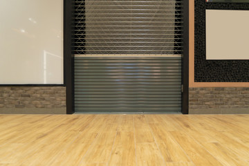 Retail shop or store closing. Steel metal roller shutter door in shopping mall with wooden floor...
