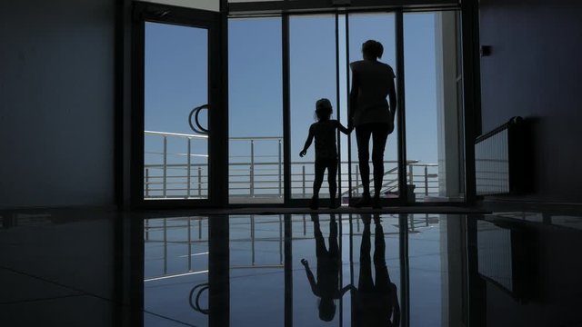 A woman with a small daughter go through the glass doors of the hotel to the promenade with a beautiful view of the sea.