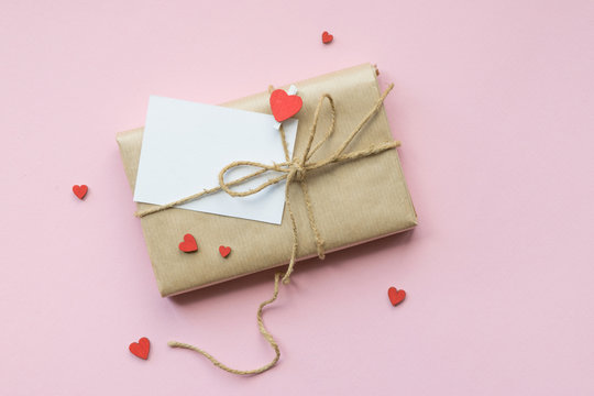 Present wrapped in brown craft paper and tie hemp string on Light pink background. Romantic Gift with decorative red hearts. Top view.
