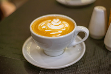 white porcelain cup of coffee or cappuccino with a pattern on the foam on a table in a cafe