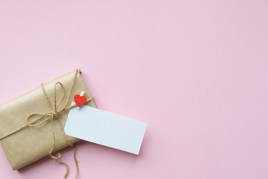 Present wrapped in brown craft paper and tie hemp string on Light pink background. Romantic Gift with decorative red hearts. Top view.