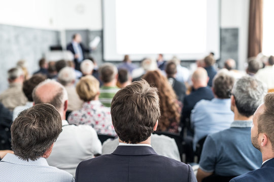 Speaker giving a talk in conference hall at business event. Audience at the conference hall. Business and Entrepreneurship concept. Focus on unrecognizable people in audience.