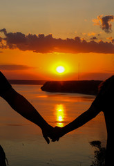 Silhouette of romantic couple holding hands on the beach and looking at sunset over the sea, love and vacation concept, warm summer, view from back