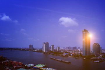 Naklejka premium Wide scene drone picture of high angle view group of home and Chaopraya river in Bangkok the capital city of Thailand with sand container tugboat and colorful morning sunrise background.