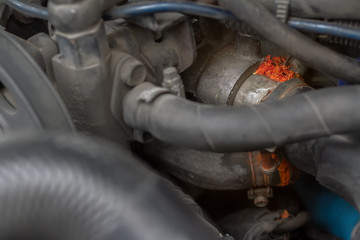 Close up leaked rusty from weathered liquid coolant pipe of cooling system under the air intake manifold sensor in an old car engine background.