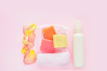 White cosmetics bottle, soap, rose petals and towel  on pink background. Concept of natural spa cosmetics. Flat lay, top view, copy space .