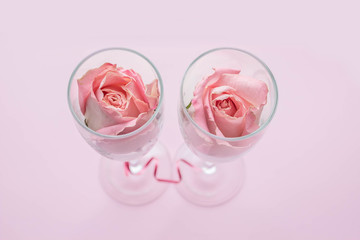 Rose buds in wineglasses on a pink background.  Background for holiday, birthday, wedding, Valentine's day, Women's Day. Top view, flat lay composition. Copy space for text or design.