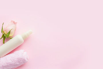 White cosmetics bottle, rose and towel  on pink background. Concept of natural spa cosmetics. Flat lay, top view, copy space .
