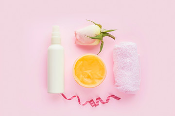 Open jar of cosmetic cream, white cosmetics bottle, rose and towel  on pink background. Concept of natural spa cosmetics. Flat lay, top view, copy space .