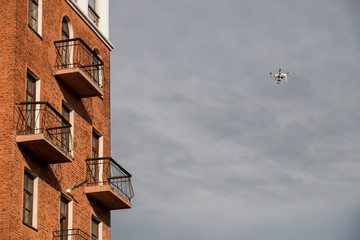 Fototapeta na wymiar Quadrocopter unmanned camera hovers in bright blue sky above city on background of urban buildings Modern technology photo and video shooting bird