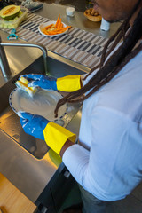 Young African-American man with dreadlocks washing in the kitchen.