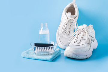 Dirty white sneakers with special tool for cleaning them on blue.