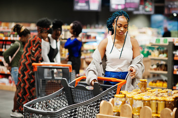African american woman choose honey pot at supermarket against her afro friends with shopping cart.