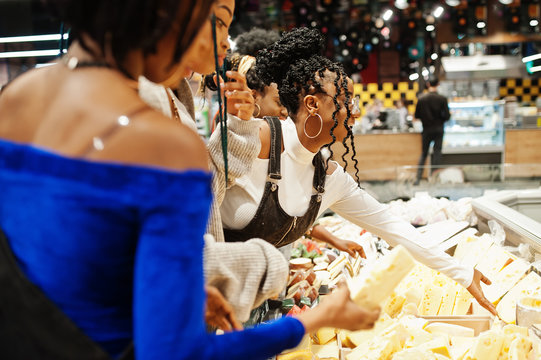 Group of five african womans with shopping carts choose cheese in supermarket.