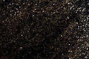 Golden glitter scattered on the black card background, top view. Abstract pattern created by hand,...