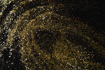 Golden glitter scattered on the black card background, top view. Abstract pattern created by hand, imitaion of storm, selective focus
