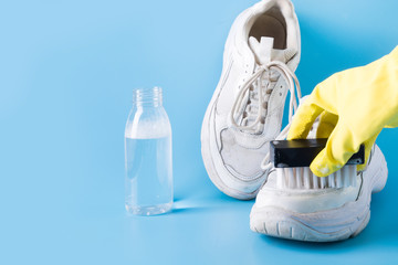 Dirty white sneakers with special tool for cleaning them on blue.