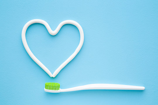 White toothbrush with green bristles on pastel blue background. Heart shape created from paste. Love healthy teeth. Empty place for text, quote, sayings or logo. Closeup.