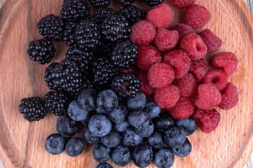 Close view on unmixed heaps of colorful berries on textured wooden plate