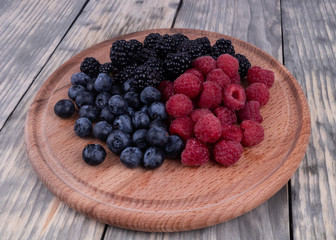 Side view on wooden plate with sumer red, blue and blackberries textured wooden background