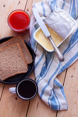 TOP VIEW OF BREAKFAST WITH COFFEE MUG, TOMATO JUICE, TOASTS AND BUTTER ON FABRIC AND RUSTIC WOODEN TABLE