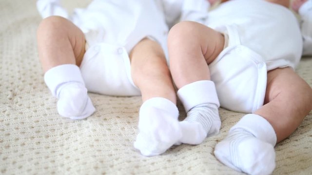 Feet Of Two Months Old Babies Wearing Socks Lying On Bed. Twins.