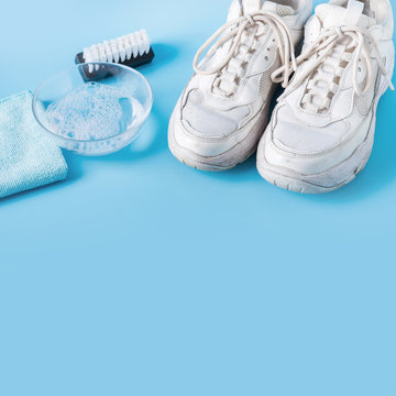 Dirty White Sneakers With Special Tool For Cleaning Them On Blue.