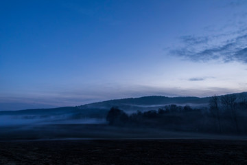 A ghostly fog hovers over farmland along a country road in New York State during a warm January evening.