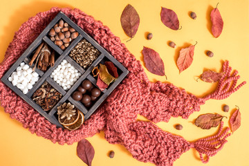 A cup of coffee, a knitted, brown scarf, cinnamon, marshmallow, multicolored sweets, anisetree and notebook on a blue, wooden background. Drinks and sweets. Top view. Copy space