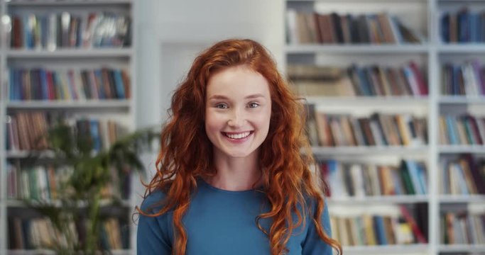 Close up of the young Caucasian charming and beautiful red-haired happy woman laughing to the camera in the library. Portrait.