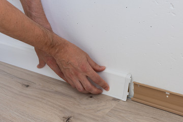 Worker installing plastic skirting board, repair work in the house