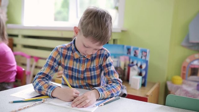 School Preparation Preschool. 6 years old boy in a class at a school desk performs an assignment in a notebook.