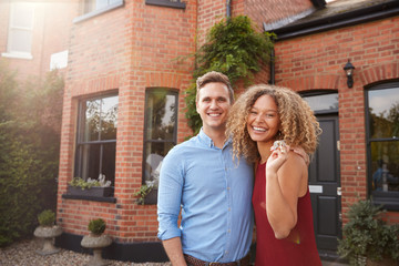 Portrait Of Excited Young Couple Standing Outside New Home Together