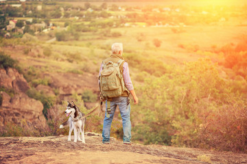 Tourist man with a gray beard with his dog breed of husky against the backdrop of trees, gorges and stones, concept of tourism and outdoor activities in old age with animals