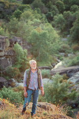 Tourist elder man with a gray beard with a backpack on his shoulders against the backdrop of the gorge, rocks and stones, the concept of tourism and outdoor activities in old age