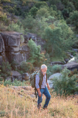 Elder man tourist with backpack is walking on rocks on the background of canyon
