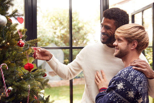 Gay Male Couple At Home Hanging Decorations On Christmas Tree Together