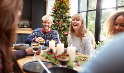 Group Of Friends Sitting Around Table At Home For Christmas Dinner Making A Toast