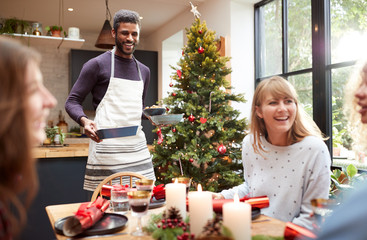 Group Of Friends Sitting Around Dining Table At Home As Christmas Dinner Is Served