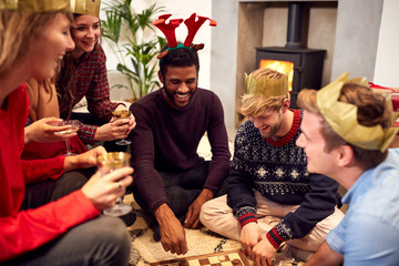 Group Of Friends Playing Board Games After Enjoying Christmas Dinner At Home - obrazy, fototapety, plakaty
