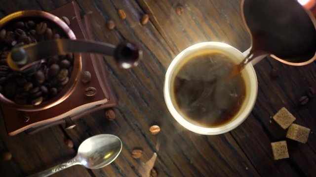 Freshly brewed coffee from cezve is poured into a coffee cup. Steam comes out of the cup, an old coffee grinder is in the composition. 4K video.