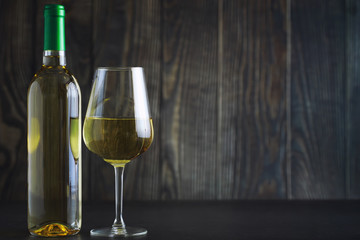 Transparent bottle of white dry wine on the table. White wine glass on a wooden background.