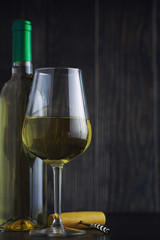 Transparent bottle of white dry wine on the table. White wine glass on a wooden background.