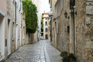Fototapeta na wymiar A deserted narrow street in an ancient city. The building is located opposite each other, between them is a narrow path lined with white stone. Porec, Croatia.