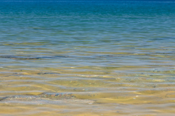 Clear water texture in blue and orange. Background of the ocean and the sea backlit by the sun. Soft waves. Natural water