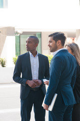 Fototapeta premium Confident business team waiting company partners outside. Business men and woman standing near office building and looking into distance. Meeting outside concept