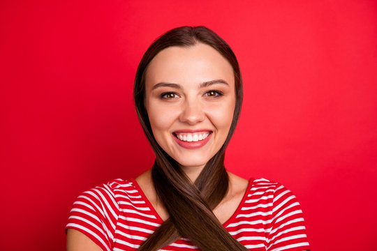 Close up photo of positive charming cute beautiful girlfriend wearing striped t-shirt showing stength of her hair while isolated with red background stretching her hair around neck