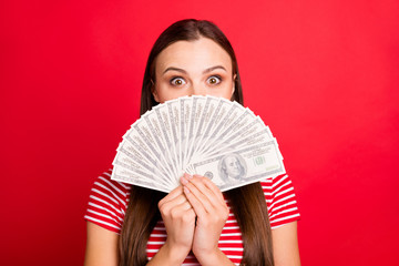 Close up photo of beautiful cute girl wearing striped t-shirt holding money with her hands hiding behind it while isolated with red background