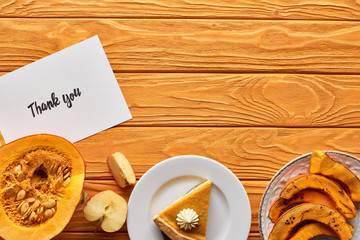 top view of delicious pumpkin pie, apples and thank you card on wooden orange table